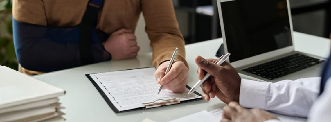 Close up of man filling in medical insurance form Close up of man filling in medical insurance form, injured hand in sling in background, copy space